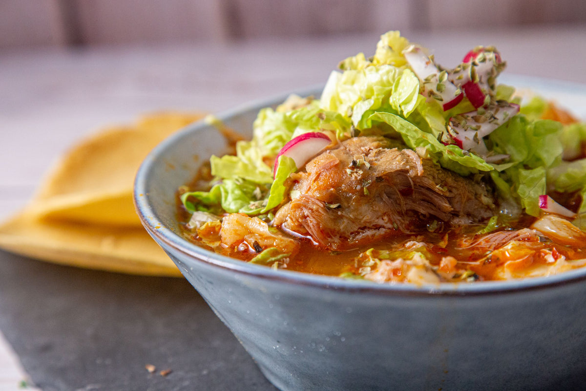 A bowl of red pozole with shredded meat, lettuce and radish